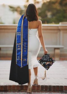 a woman in a white dress is holding a black and blue graduation stole with writing on it