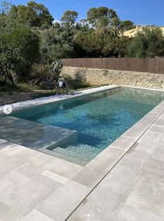 an empty swimming pool in the middle of a backyard with stone walls and trees around it