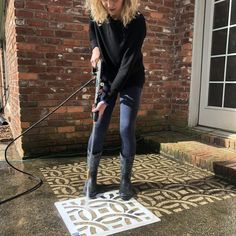 a woman in black shirt and jeans holding an ironing board on sidewalk next to brick building