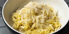 a white bowl filled with pasta and parmesan cheese on top of a table