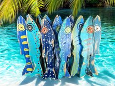 four wooden fish are lined up in the water near some palm trees and blue water