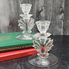 two clear glass candlesticks sitting on top of a table next to a book