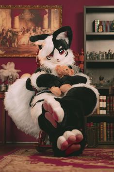 a cat sitting on top of a chair holding a teddy bear in it's paws