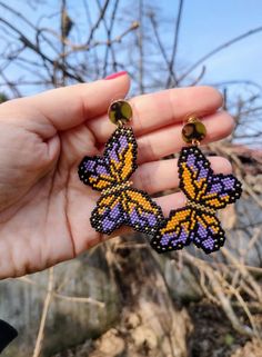 a person holding two small butterfly shaped earrings in their left hand, with trees in the background