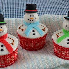 four cupcakes decorated with snowmen sitting on top of a blue and white table cloth