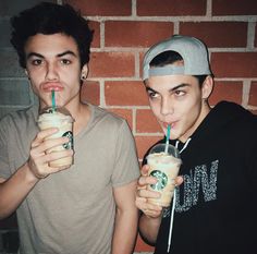 two young men holding drinks in front of a brick wall