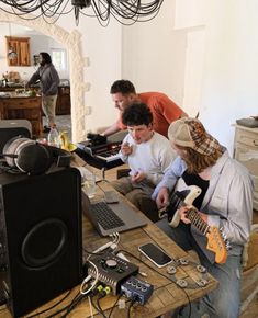 three people sitting at a table with electronic equipment on it and one person holding a guitar