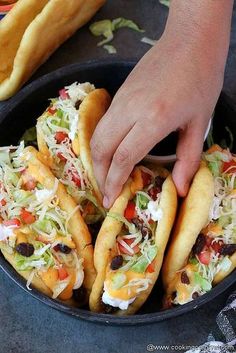 two hot dogs with toppings in a pan being held by someone's hand