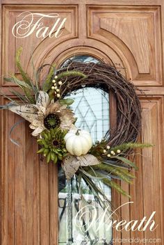 a wreath with white pumpkins and greenery hangs on the front door of a house