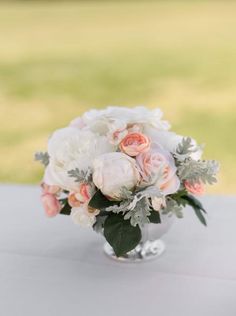 a vase filled with white and pink flowers on top of a table next to a green field