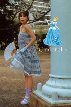 a woman in a blue dress is standing next to a pole and holding an umbrella