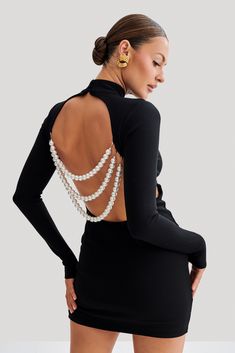 a woman in a short black dress with pearls on the back and her hands on her hips