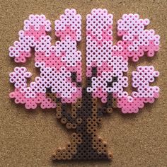 a tree made out of perler beads on a corkboard background, with pink flowers in the center