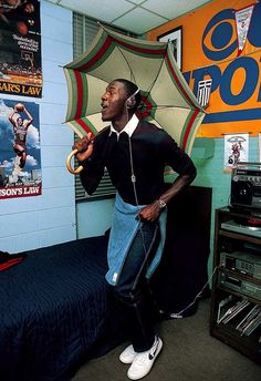 a man standing next to a bed in a room with posters on the wall and an umbrella over his head