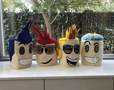 four different colored pencil holders with faces painted on them sitting on a window sill