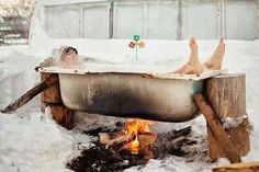 two people laying in a bathtub next to an open fire with snow on the ground