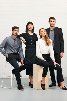 four people are posing in front of a white brick wall and one person is sitting on a chair