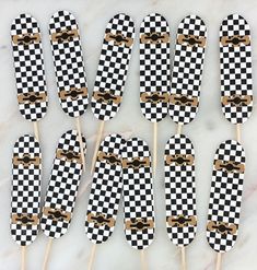 six black and white checkered toothpicks with gold bows on them sitting on a marble surface