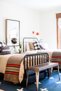 a bedroom with two beds and a bench in the foreground, one bed has a plaid blanket on it