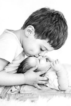 a black and white photo of a young boy kissing his newborn baby's face