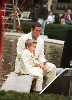 a man in a white suit sitting next to a little boy