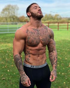 a man with tattoos on his chest standing in the grass