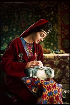 a woman is sitting down with a rabbit in her lap and wearing a red outfit