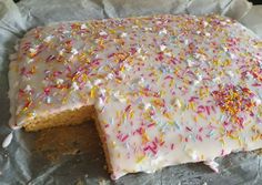 a cake with white frosting and sprinkles on it sitting on top of a piece of wax paper