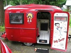 an old red trailer with the door open and cartoon characters painted on it's side