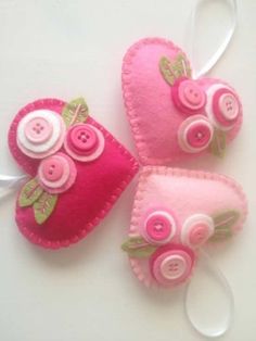 three pink felt heart ornaments with buttons and flowers on them, hanging from a white ribbon