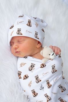 a baby wrapped in a blanket with a teddy bear on it's head and wearing a white hat