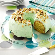 a cake with green frosting and nuts is on a plate next to a knife