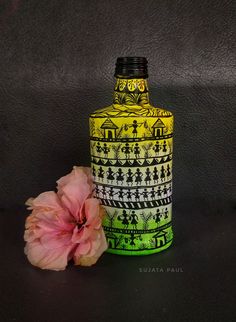 a yellow and green vase sitting next to a pink flower on a black tablecloth