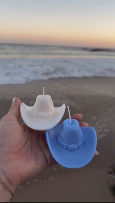 a hand holding a toy cowboy hat on top of a blue plastic object in front of the ocean