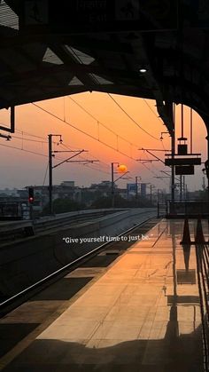 the sun is setting at an empty train station