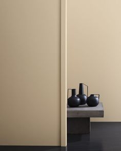 three black vases sitting on top of a wooden table next to a white wall