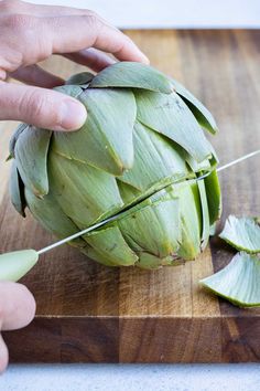 a person cutting artichoke on a wooden cutting board