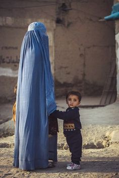 a little boy standing next to a woman wearing a blue shawl and holding the hand of another child