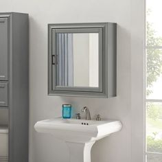 a white sink sitting under a mirror next to a gray cabinet in a bathroom near a window