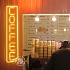 a man standing in front of a counter with coffee cups on it and a neon sign behind him