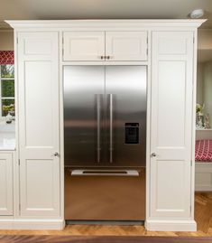 a stainless steel refrigerator in a kitchen with white cabinets and wood flooring on the side