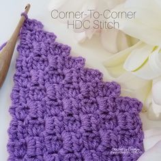 a crocheted purple square sits next to white flowers