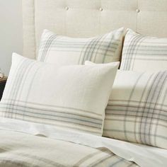 a bed with white and blue plaid pillows on it's headboard next to a night stand