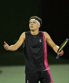 a man holding a tennis racquet on top of a tennis court at night