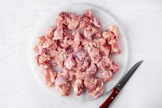 chopped meat on a white plate next to a knife and pepper shaker with red handled utensils