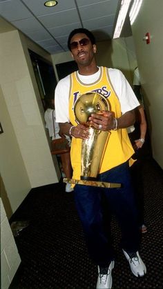 a man in a yellow shirt holding a trophy and wearing white converse shoes with sunglasses on his head