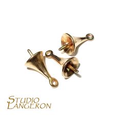 two brass bell charms sitting side by side on a white background with the words studio langeron written below them