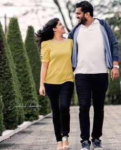 a man and woman are walking down the sidewalk together, smiling at each other as they hold hands