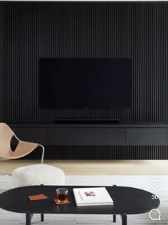 a living room with a black coffee table and white chairs in front of a flat screen tv