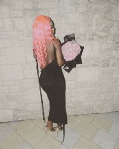 a woman with pink hair holding a bouquet of flowers in front of a brick wall